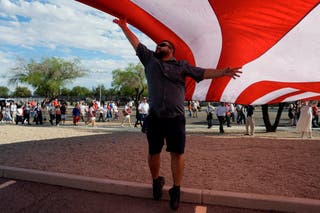 A man helps display a U.S. flag outside State Farm Stadium, on the day of a memorial service for slain conservative commentator Charlie Kirk takes place, in Glendale, Arizona, U.S., 21 September 2025